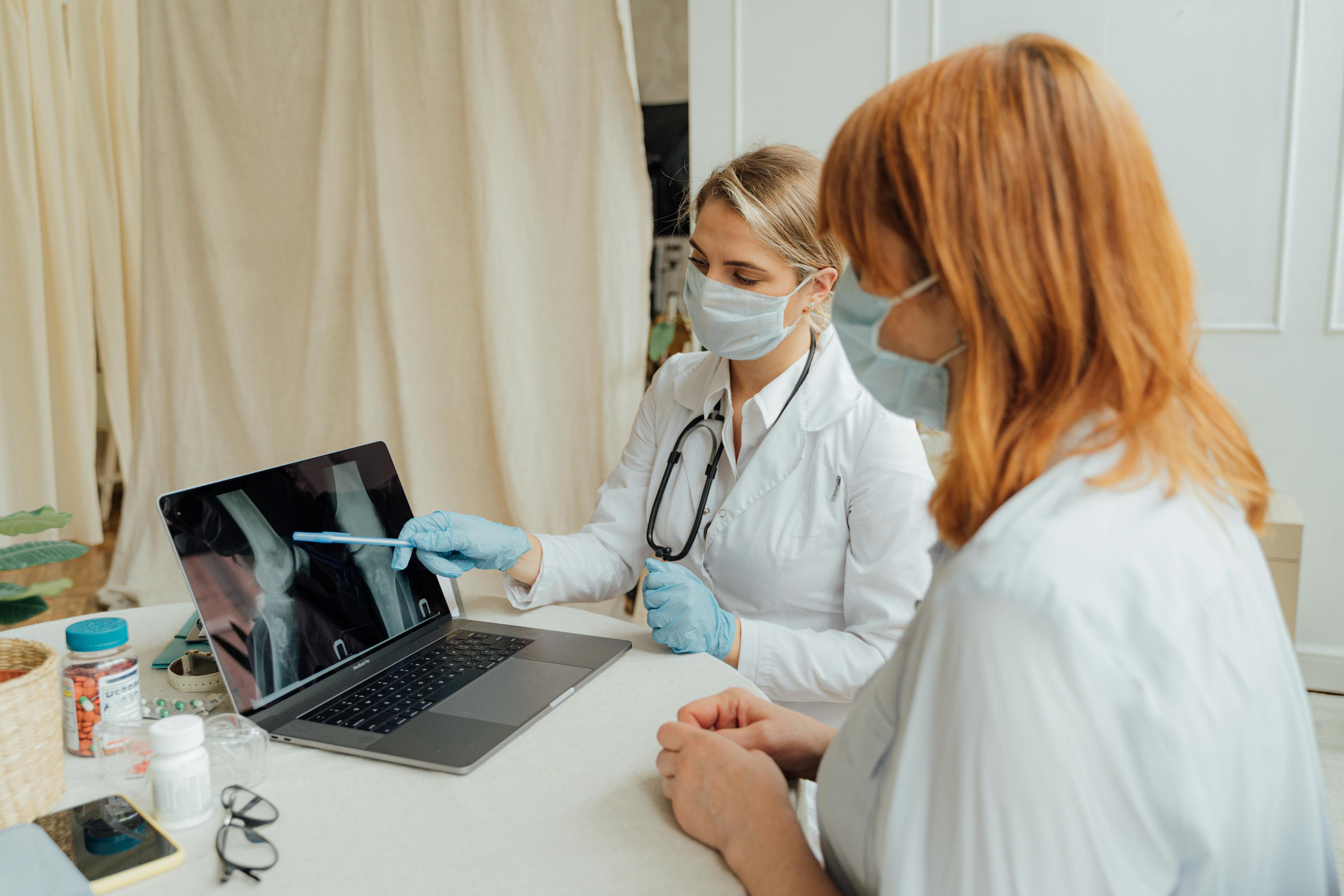 Doctor pointing to a laptop, explaining something to a patient sitting with them.